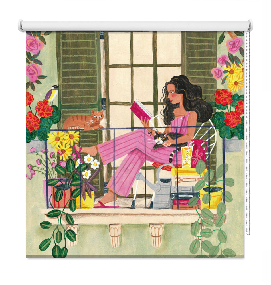 Printed roller blind featuring a colourful illustration of a woman reading a book on a balcony surrounded by potted plants, flowers, a cat, and green shutters