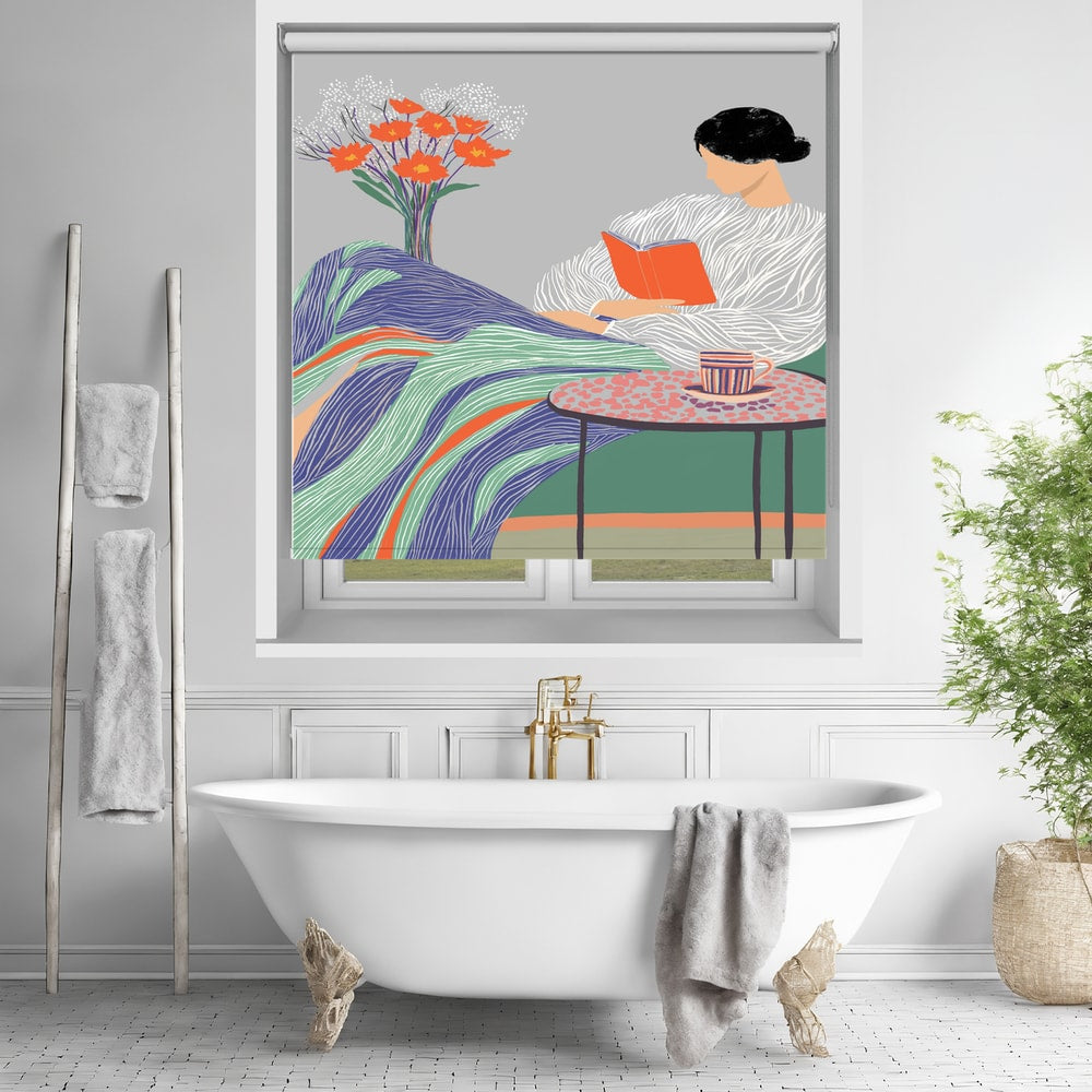 Printed roller blind featuring a graphic illustration of a woman reading an orange book under a colourful wavy blanket with a coffee cup and orange flowers nearby