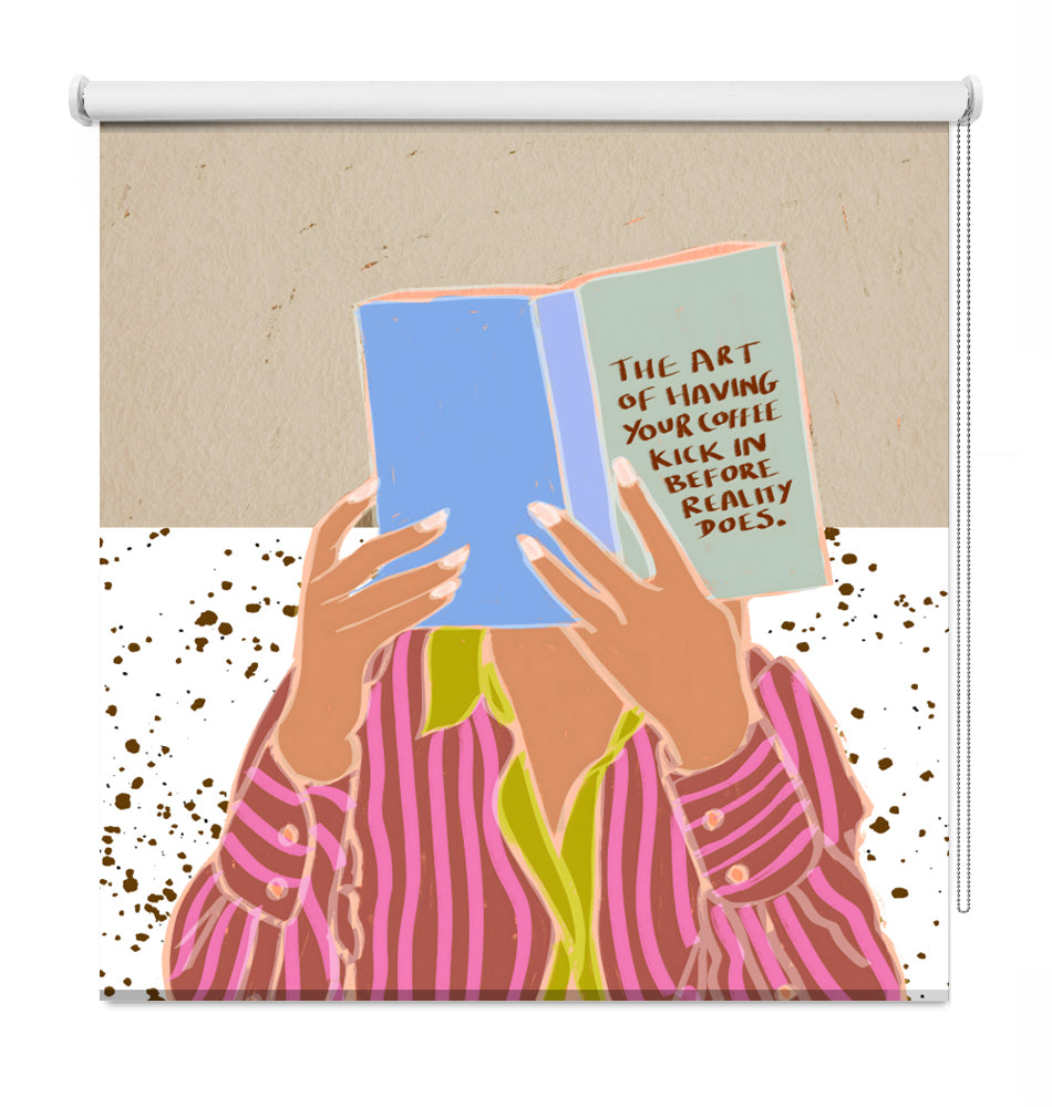 A decorative window roller shade featuring a colorful graphic illustration of a person in pink striped pajamas holding a blue book with a quote on the cover, set against a beige and white background with brown speckles.