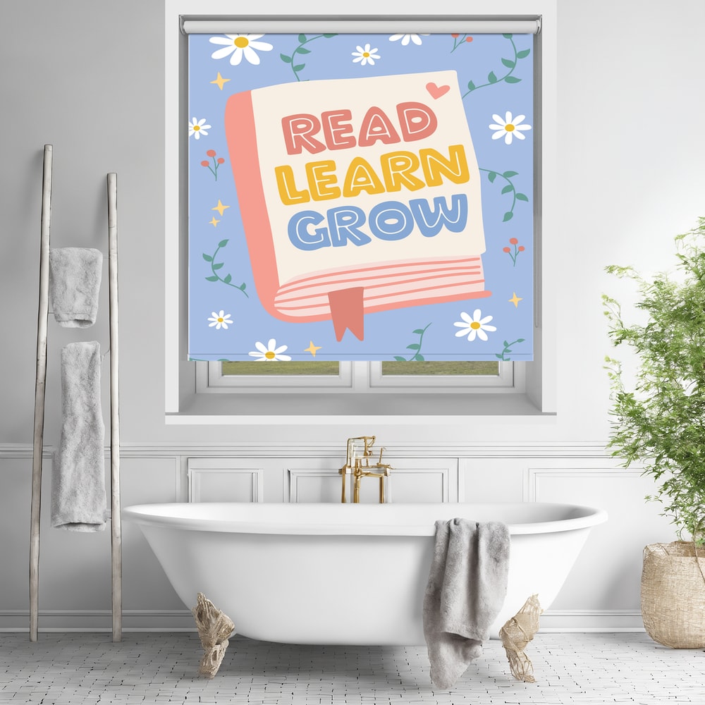Printed roller blind featuring a pink book with the text Read Learn Grow surrounded by white daisies on a blue background, hanging over a white freestanding bathtub