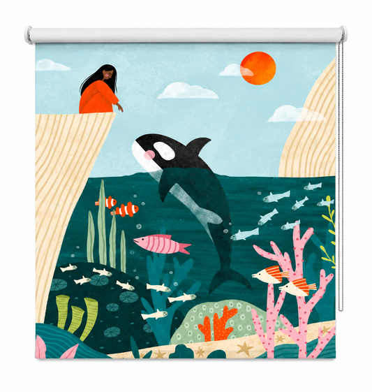A stylized illustrated ocean scene printed on a window roller shade, showing an orca, fish, coral, a person in an orange dress on a cliff, clouds, and a sun in a flat, colorful art style.