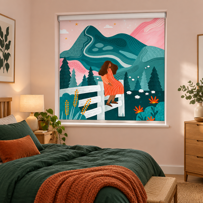 A roller shade with a colorful illustrated print of a woman on a fence in front of mountains and trees, shown installed in a styled bedroom with a bed, lamp, and dresser.