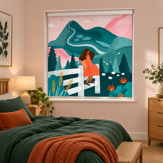 A roller shade with a colorful illustrated print of a woman on a fence in front of mountains and trees, shown installed in a styled bedroom with a bed, lamp, and dresser.