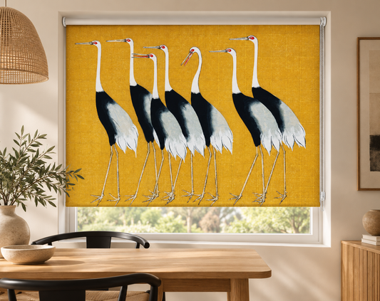 A window roller shade featuring a printed design of seven storks on a mustard yellow background, shown installed in a modern dining room setting.